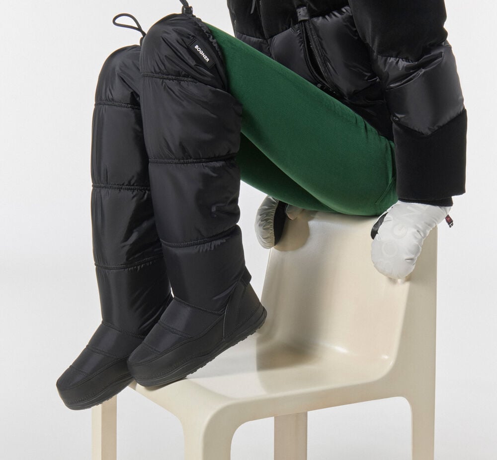 Schwarze, gesteppte Overknee-Boots, kombiniert mit einer Steghose, schwarzer Daunenjacke und weißen Handschuhen.