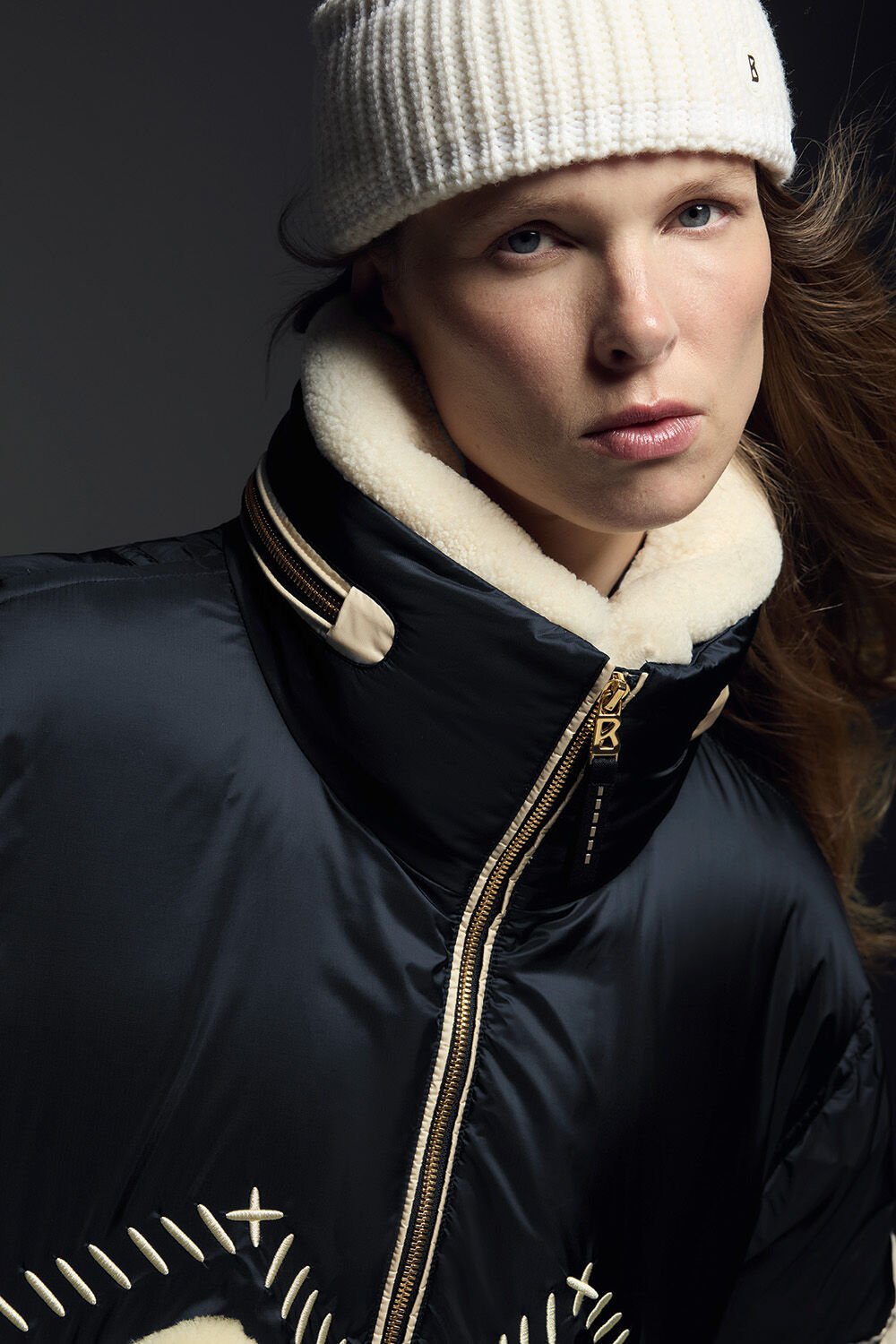 Close-up von einer schwarzen bestickten Skijacke mit Shearling-Kragen und goldfarbenem B-Zipper.