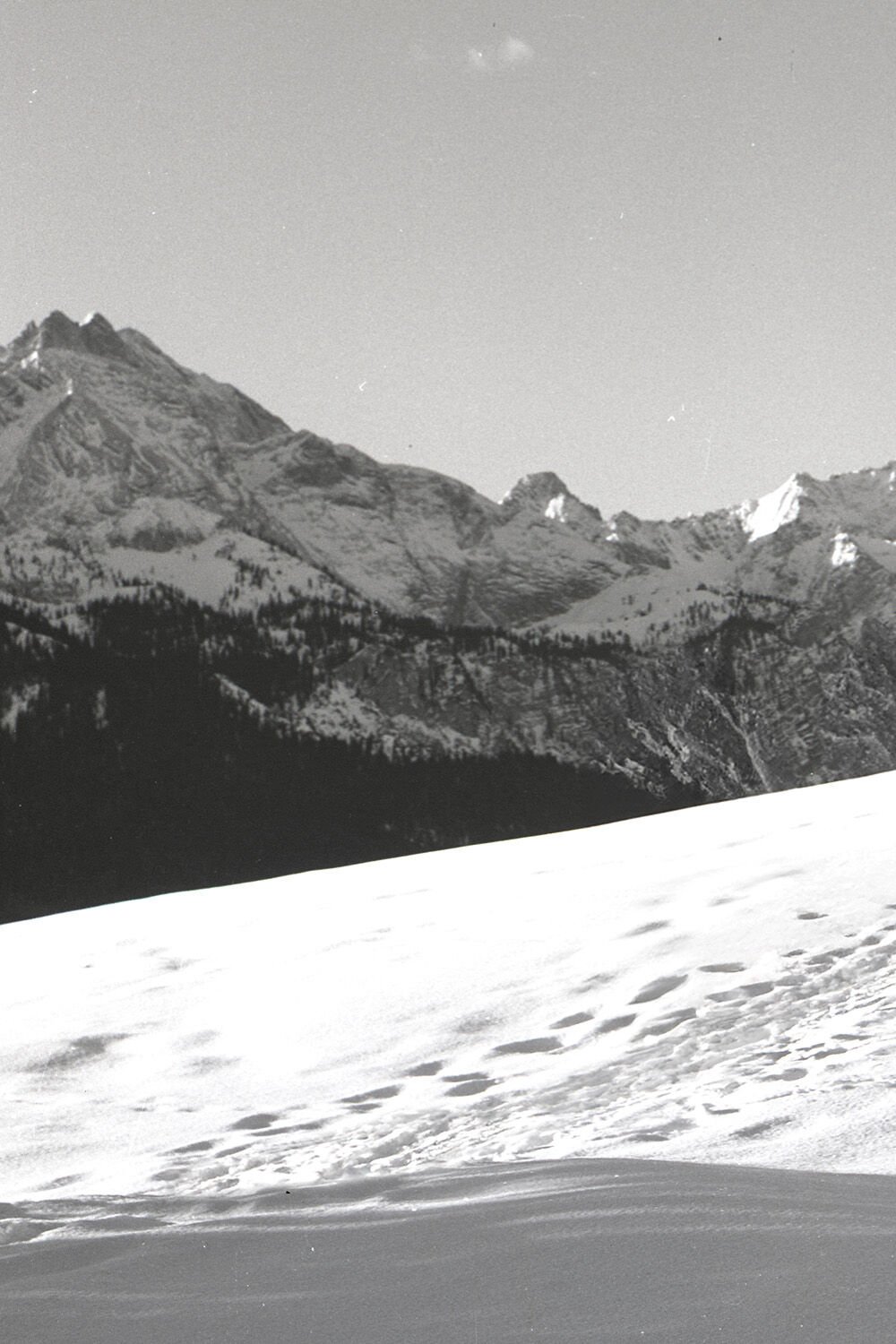 Zu sehen ist ein Schwarz-Weiß-Motiv einer schneebedeckten Berglandschaft.