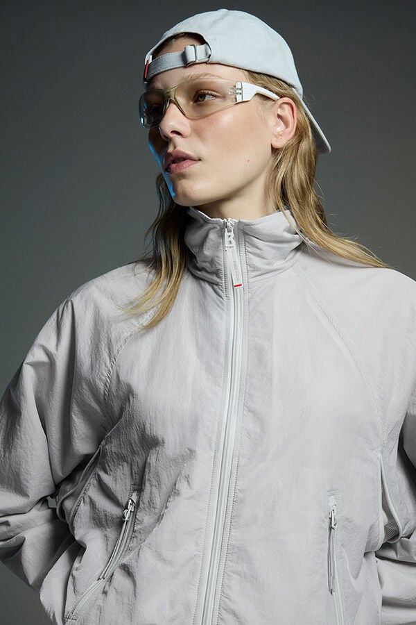 Close-up des Damen Models mit Funktionsjacke Yosefine in Hell-Grau. Dazu tr&auml;gt sie eine Cap und eine Sonnenbrille.