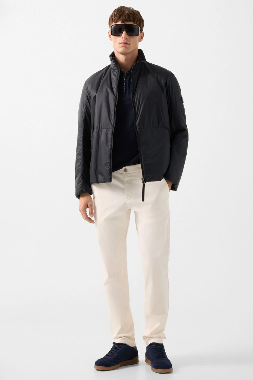 The male model is wearing the cream-colored Jacob blouson, combined with a polo shirt in cyan blue and light-colored pants.