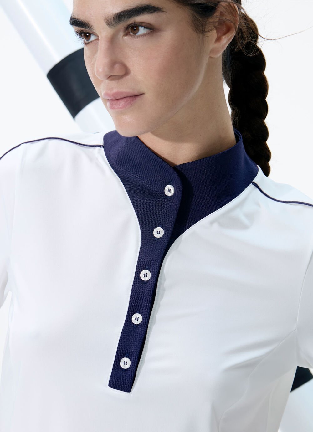 Close-up of the female model. She wears a white polo shirt with dark blue piping and button placket.
