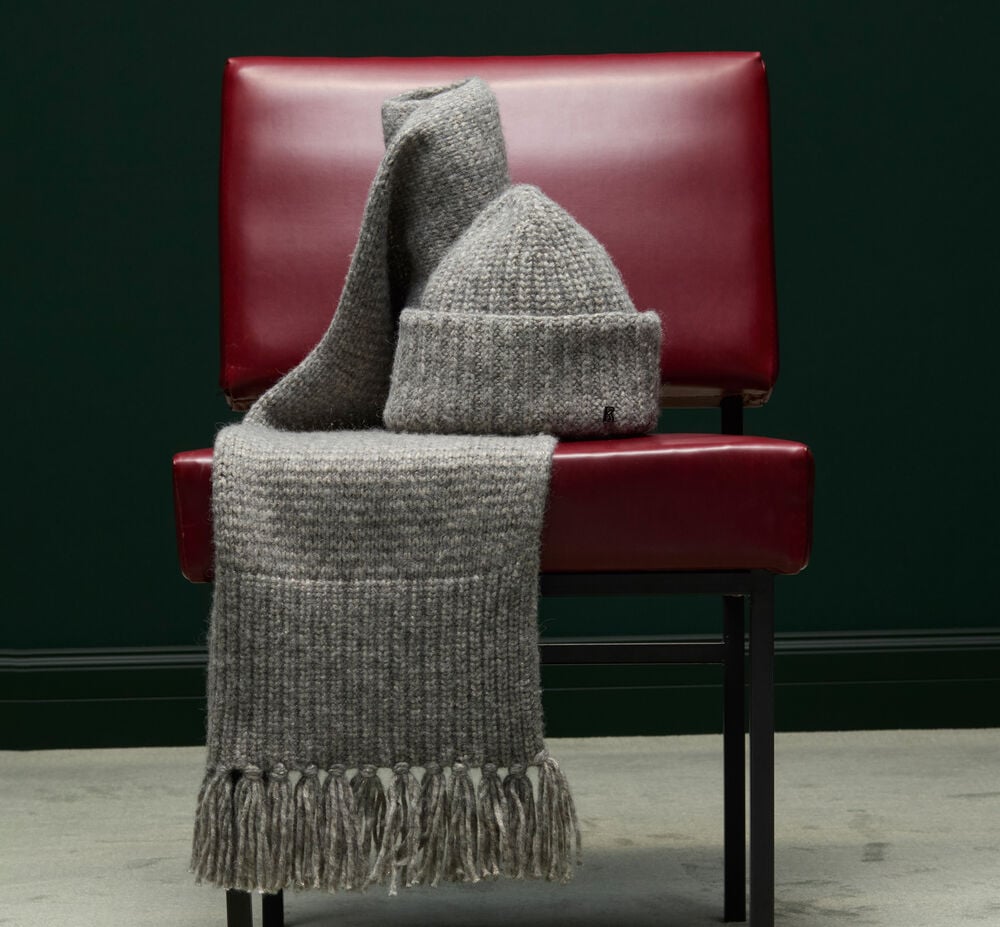 Sur un fauteuil bordeaux, un écharpe grise à franges et un bonnet côtelé sont posés avec style.