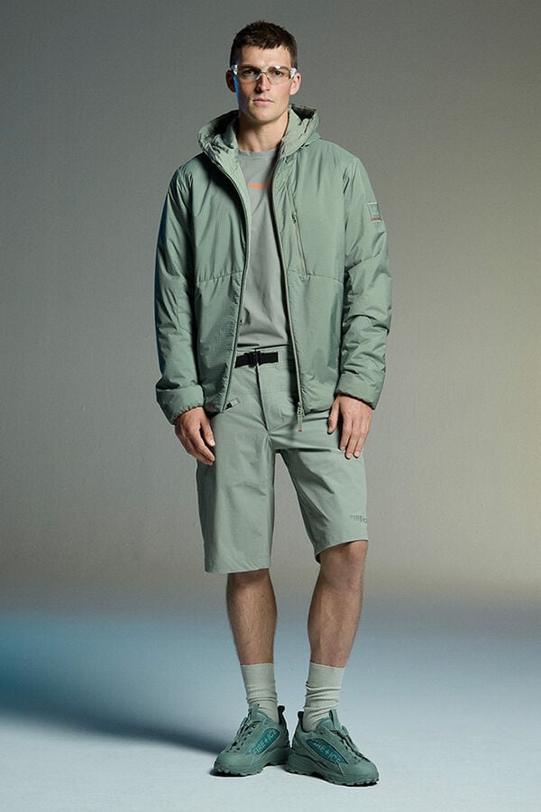 Das Herren Model tr&auml;gt einen Komplettlook in Gr&uuml;n, bestehend aus T-Shirt, wattierter Jacke und Shorts.