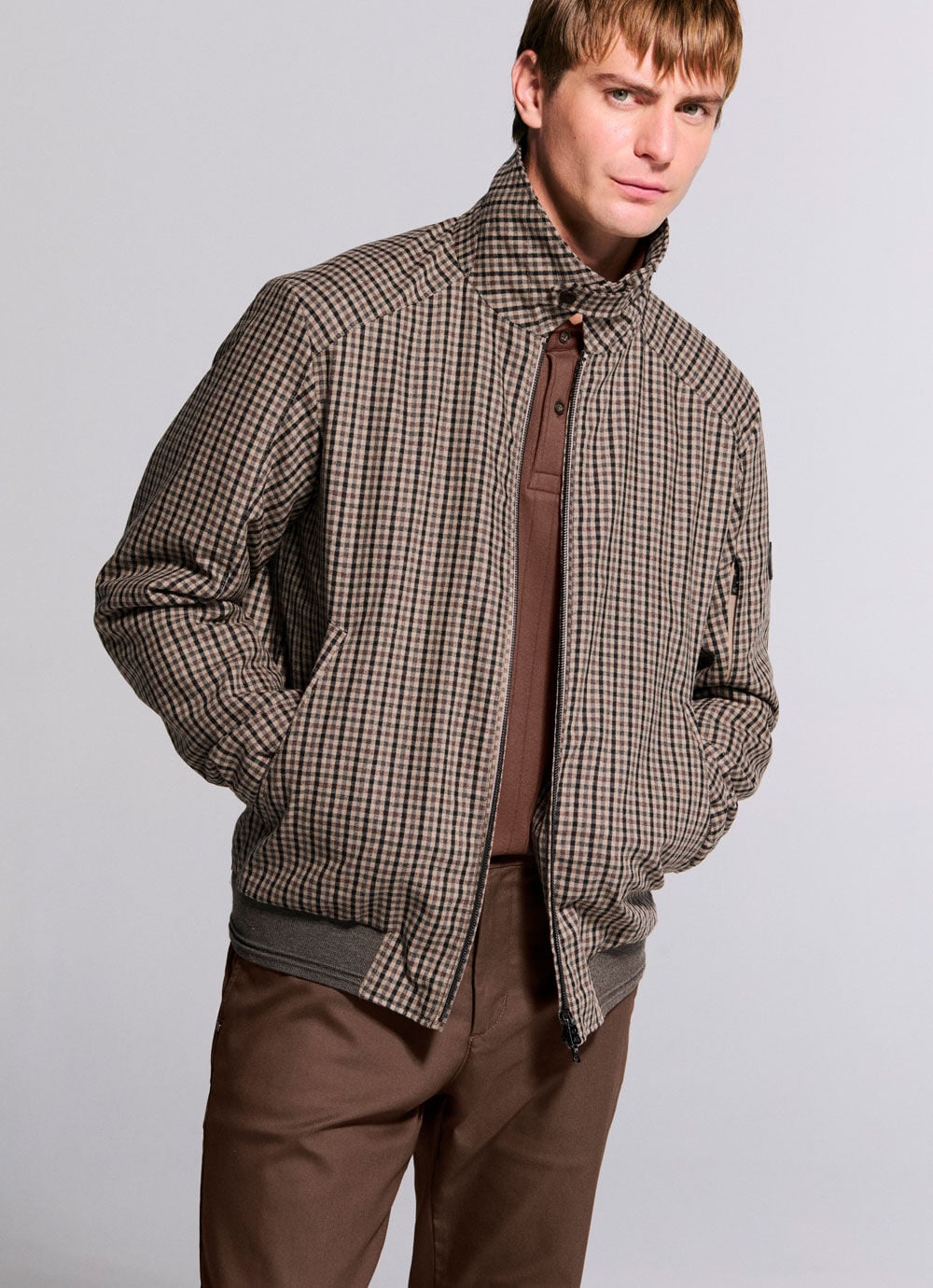 Das Herren Model tr&auml;gt die hochgeschlossene Outdoor-Jacke Amon mit Karomuster in braun-beiger Farbgebung.