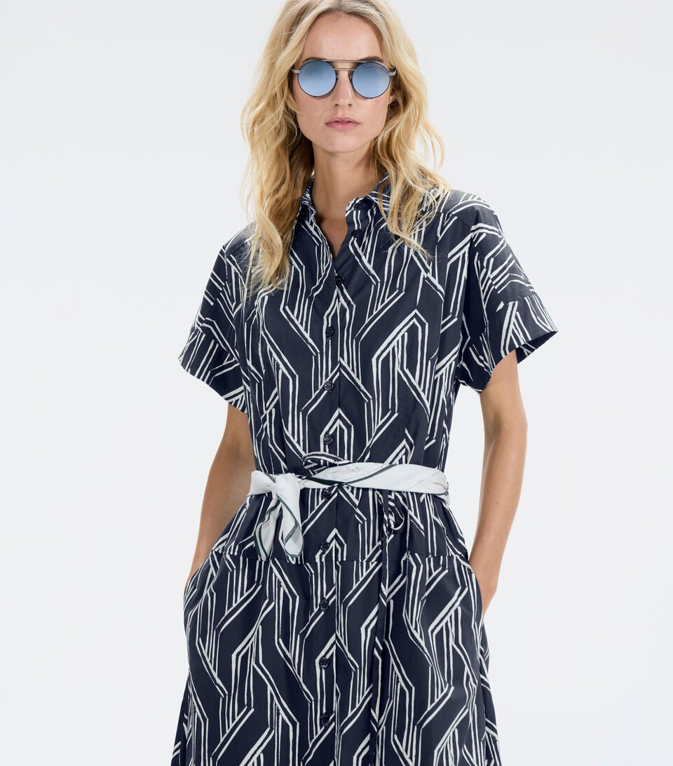 Das blonde Damen Model tr&auml;gt Hemdblusen-Kleid Roxana mit grafischem Muster in Blau und Wei&szlig;.