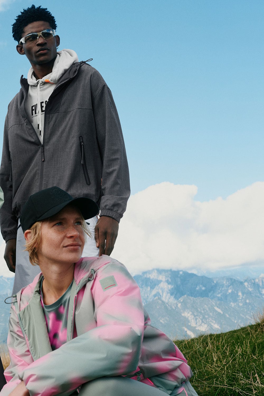 A male and female model wearing FIRE+ICE looks in anthracite, grey, pink and eucalyptus. Mountain scenery in the background.