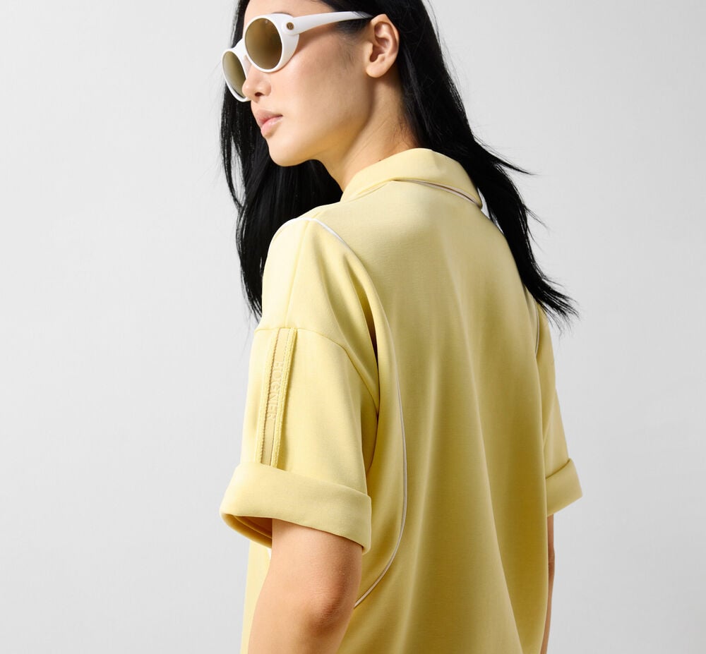 R&uuml;ckseitige Aufnahme eines Damen Models. Sie tr&auml;gt ein sonnengelbes T-Shirt und eine Sonnenbrille.