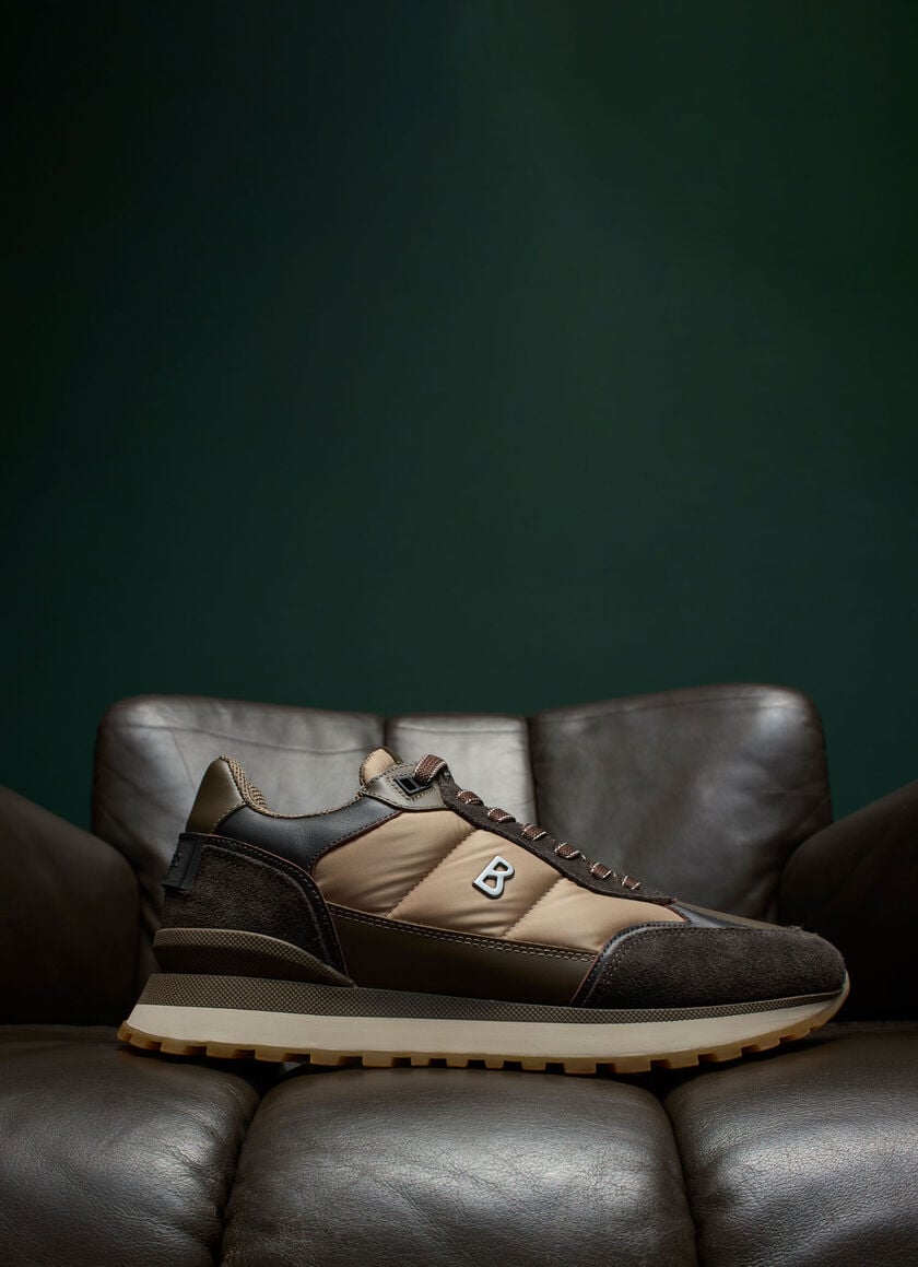 The sneaker, placed on a dark brown sofa, features a multicolored look with B detailing on the side.