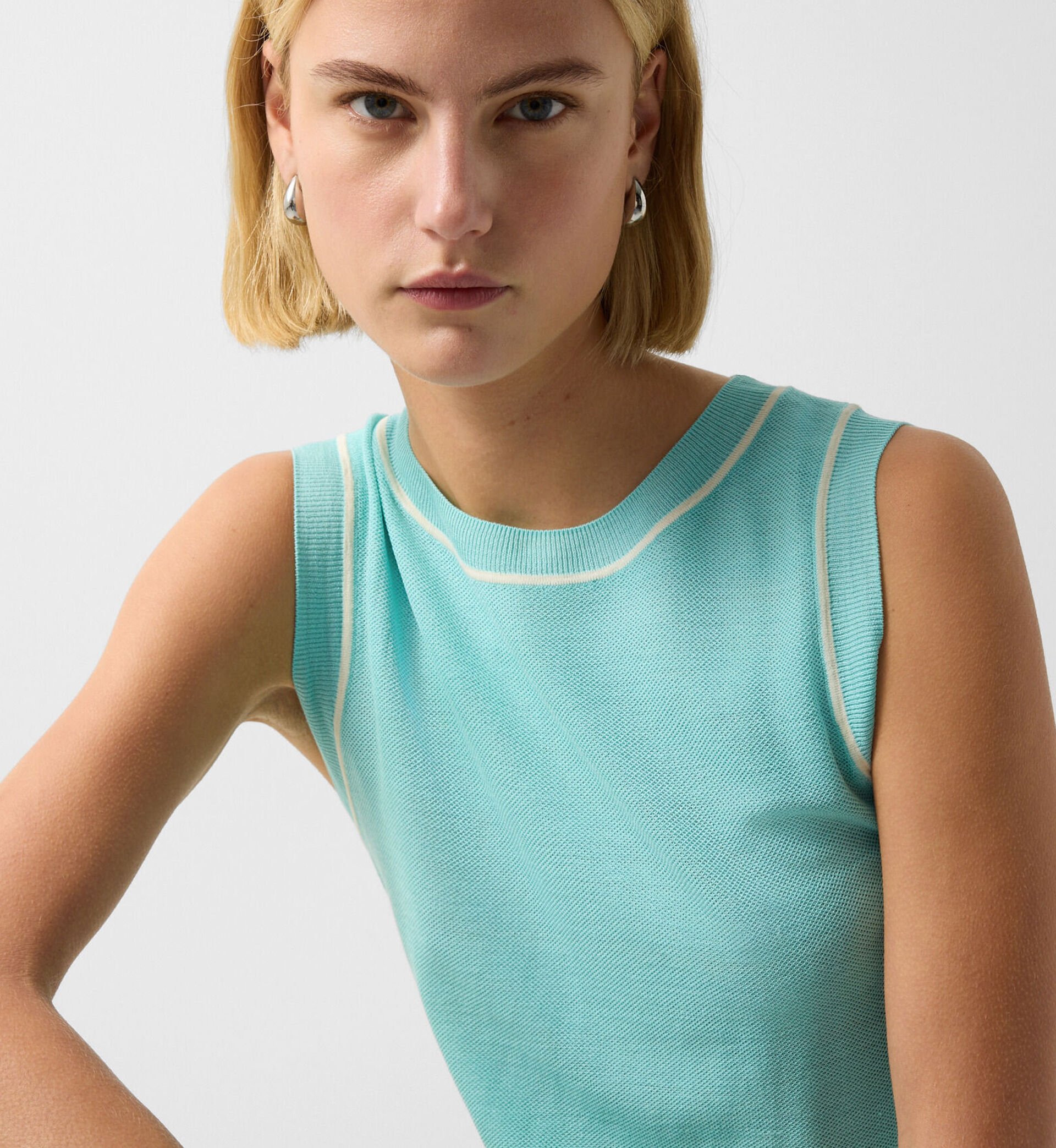 Close-up of the blond female model wearing the Phia short sleeve knitted top in cyan blue.