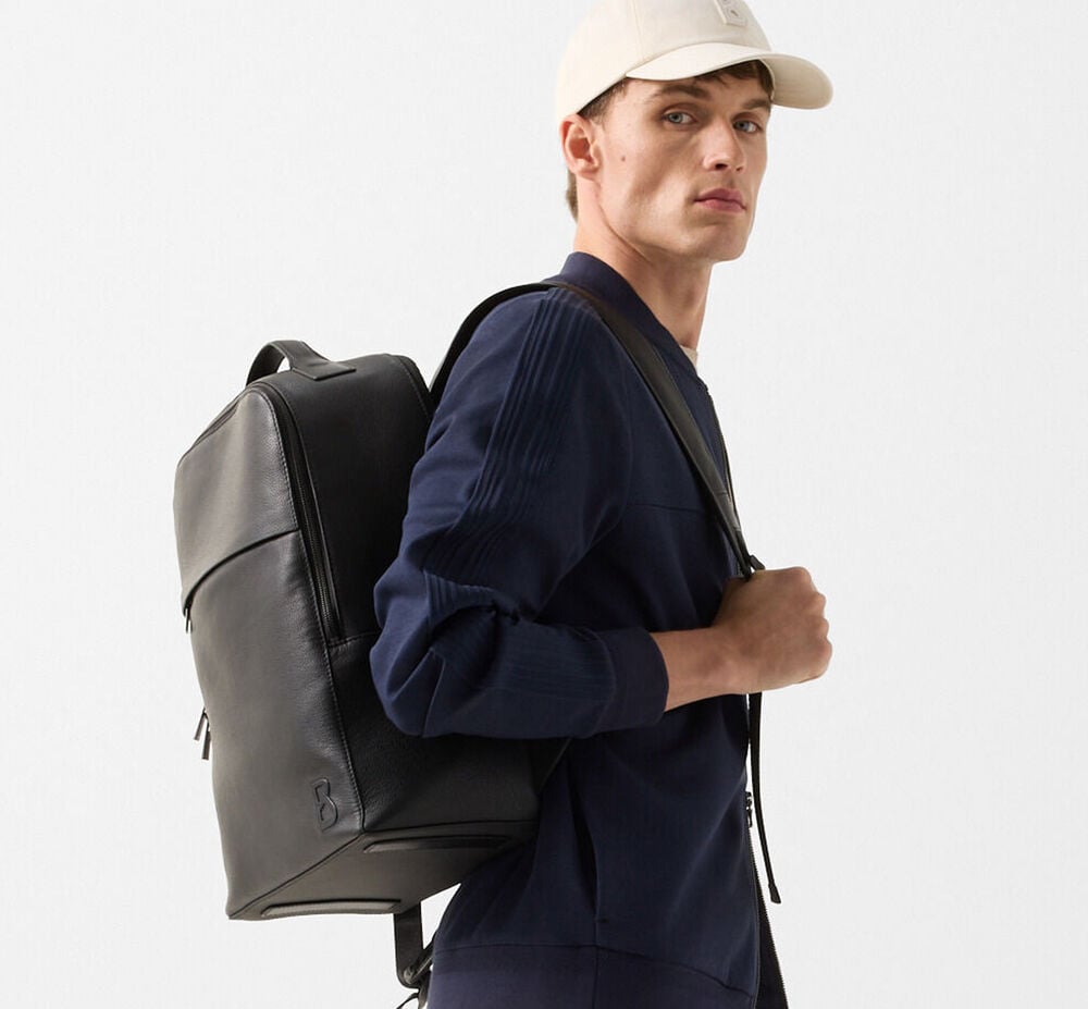 Close-up des Herren Models mit Sweatjacke Lennox in Dunkelblau. Schwarzer Lederrucksack &uuml;ber der Schulter. 