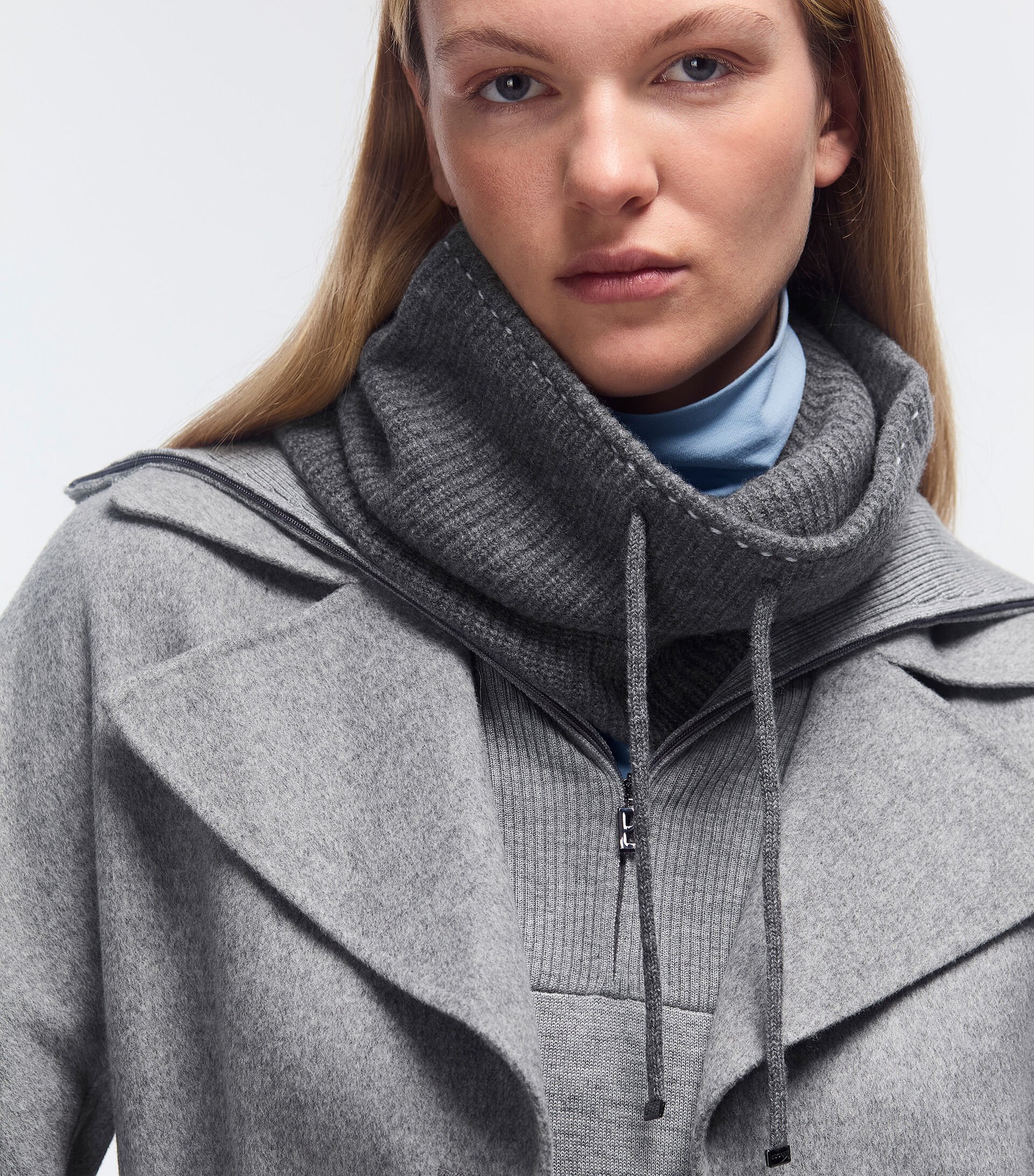 Close-up of female model. She is wearing a total look in grey: a turtleneck pullover, a knitted dress with a ‘B’ logo zip and a coat.