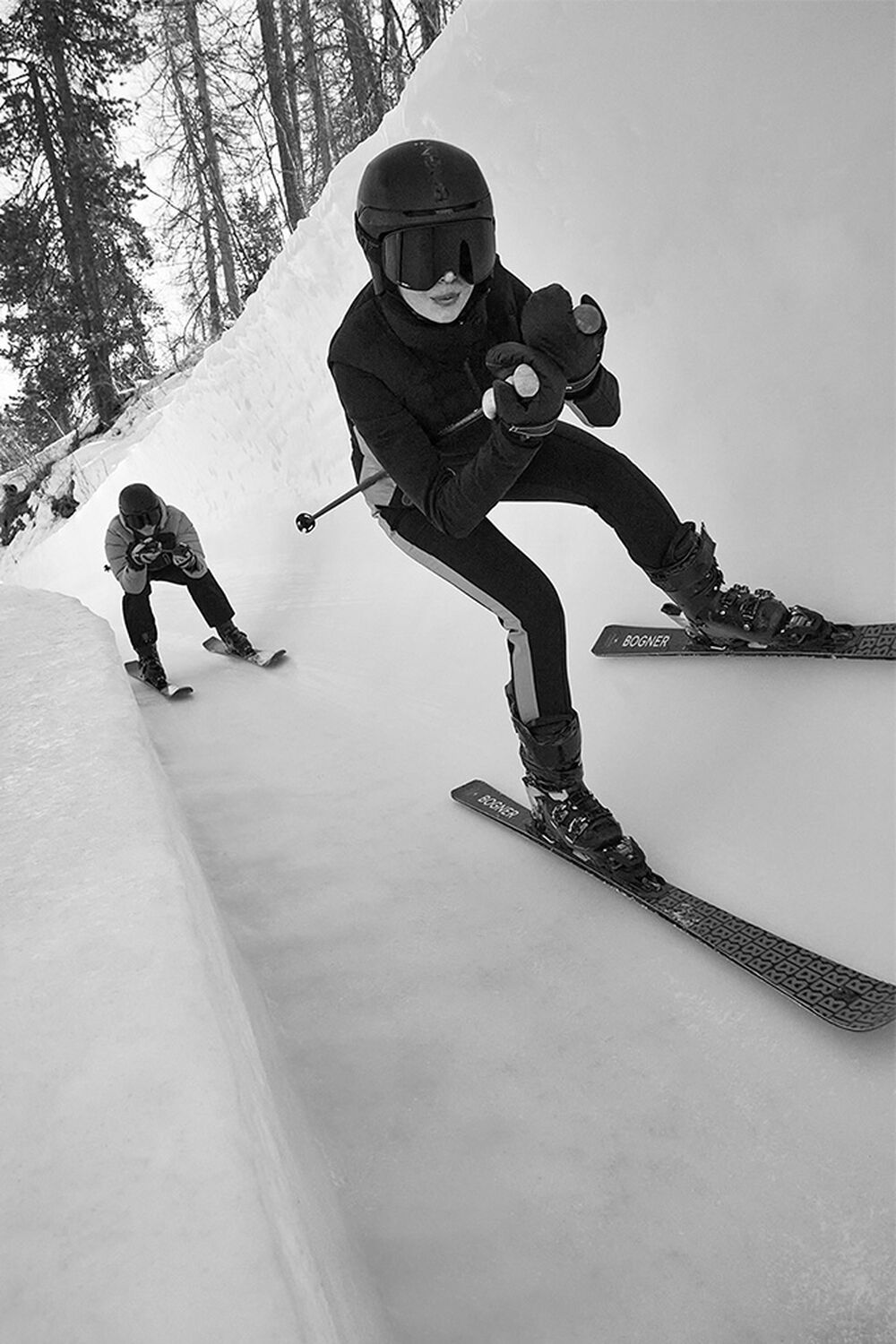 The image shows two people skiing down an ice channel in a slightly crouched position. 