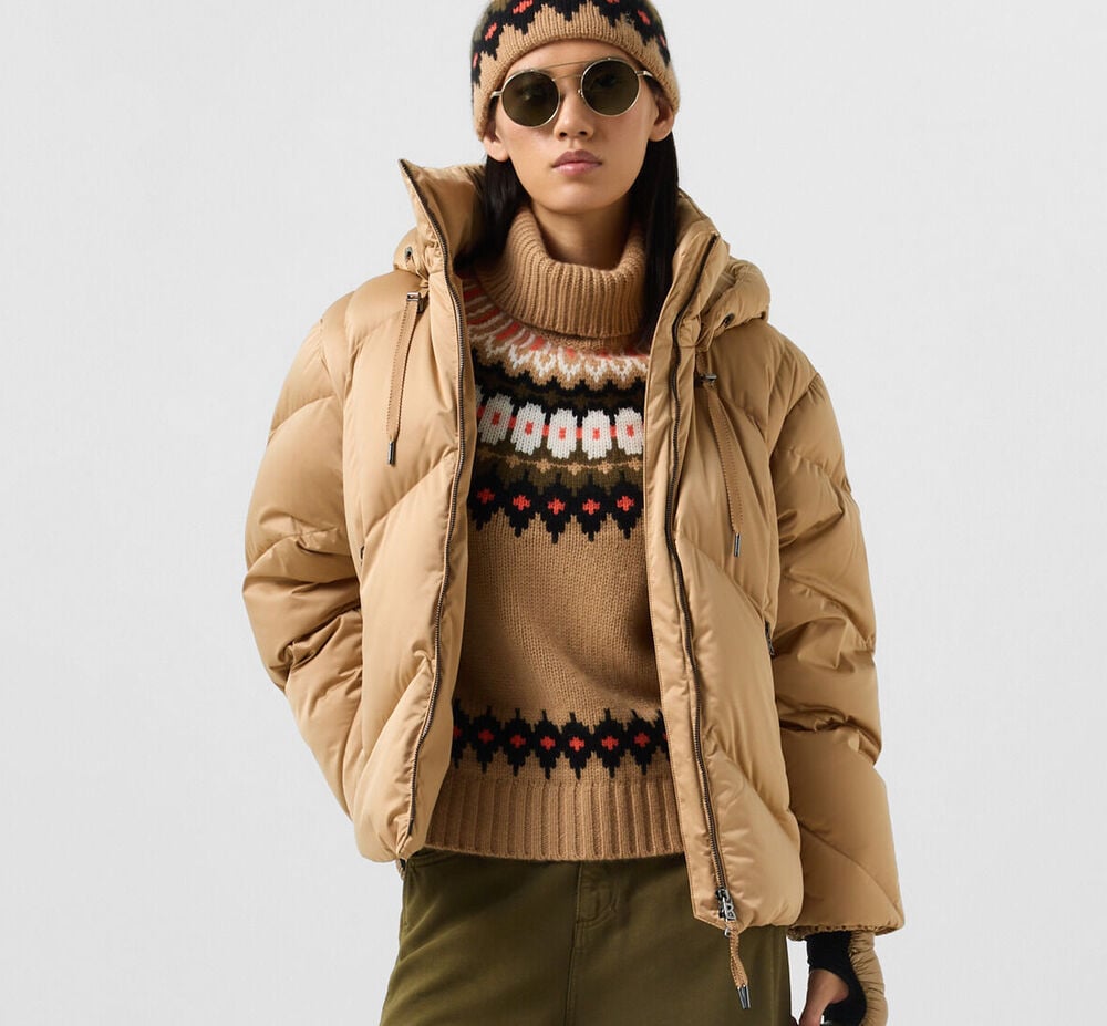 Das dunkelhaarige Damen Model tr&auml;gt Daunenjacke Georgia in Camel, darunter Kaschmir-Norweger Ingrid. Abgerundet wird der Look von Stirnband Loca und Sonnenbrille Colorado.
