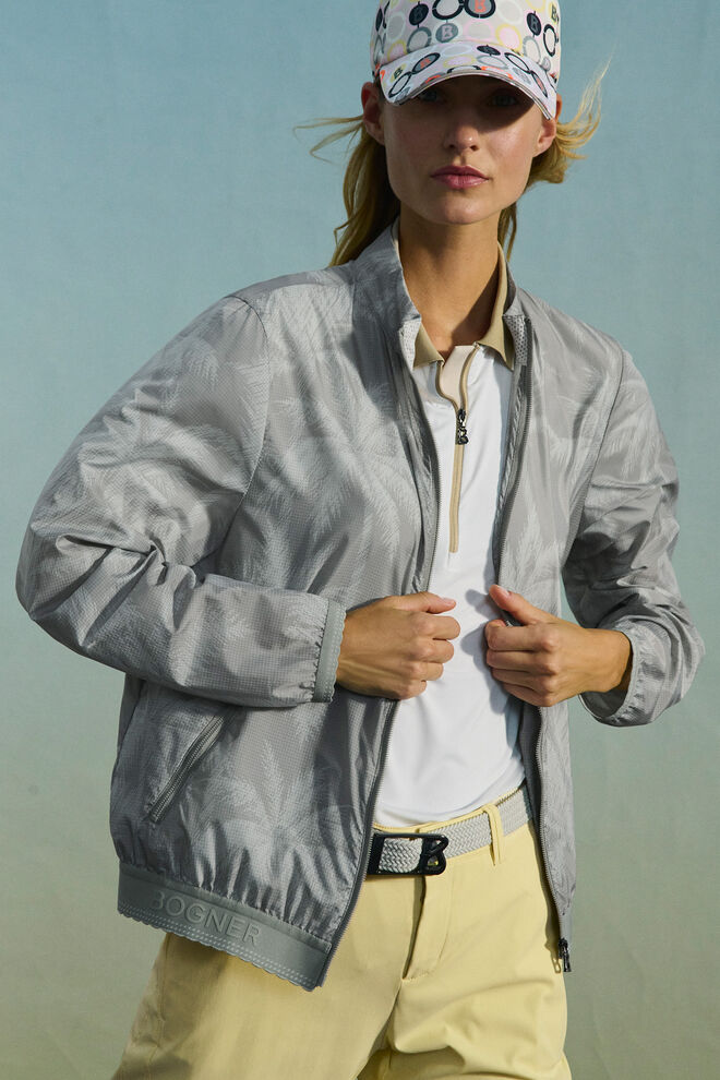 The blonde model wears the lightweight Sofie blouson in eucalyptus green, highlighted with a signature palm print.