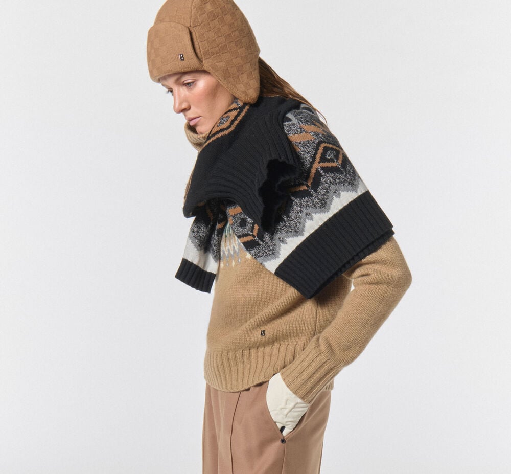 Creative styling of a Norwegian sweater wrapped around the model's neck. She is wearing a hat and a turtleneck sweater.
