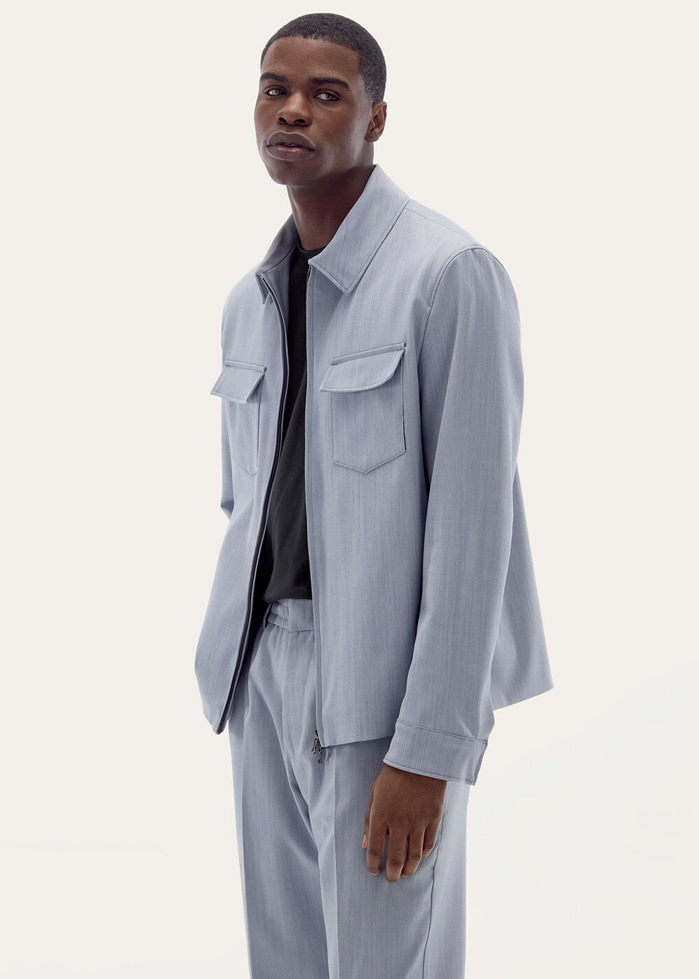 Halbkörperaufnahme. Das Herren Model trägt eine hellblaue Hemdjacke mit farblich passender Hose.