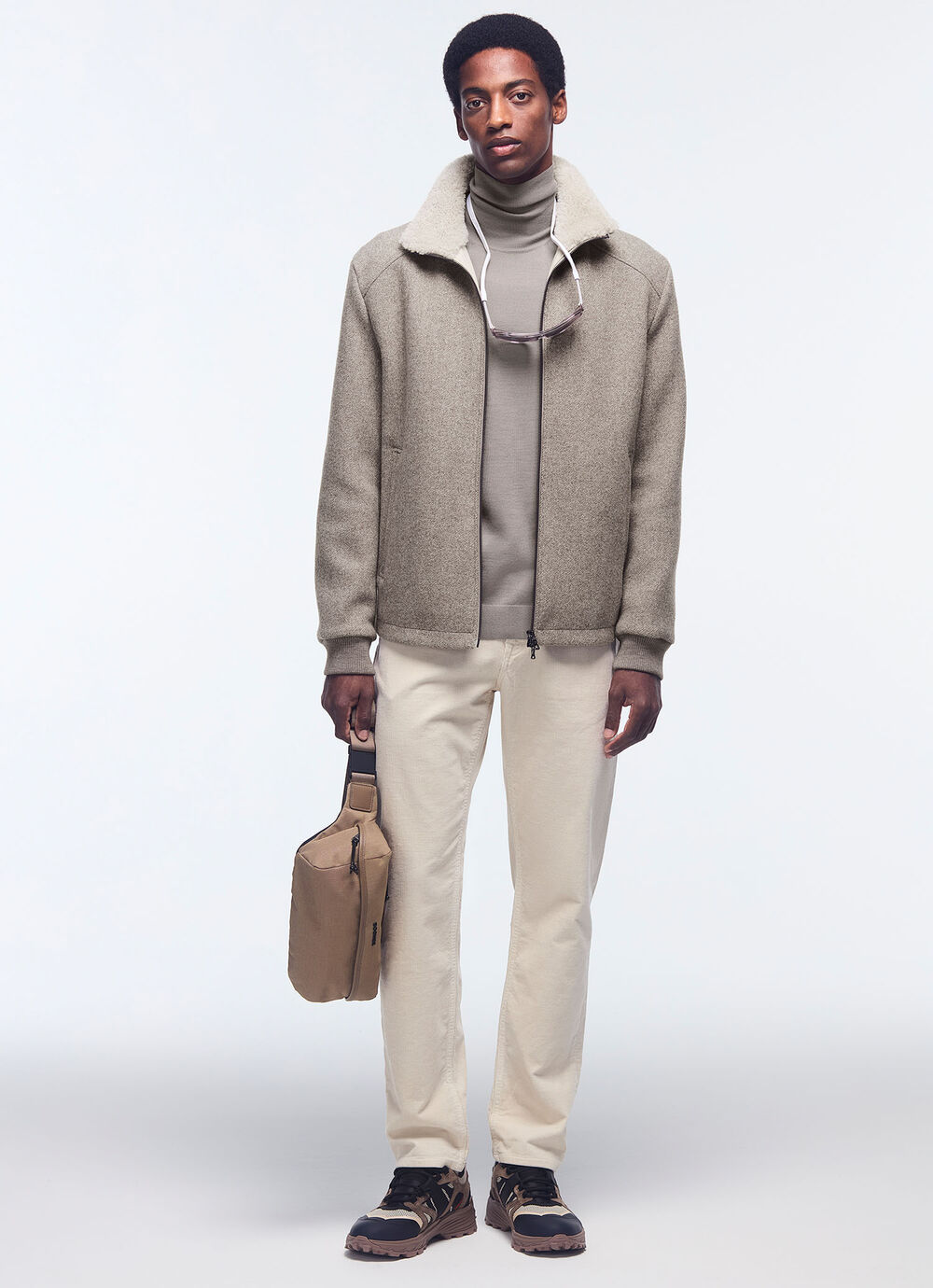 Het model draagt een beige wollen flanellen overhemd met een taupekleurige coltrui en een crèmekleurige broek.