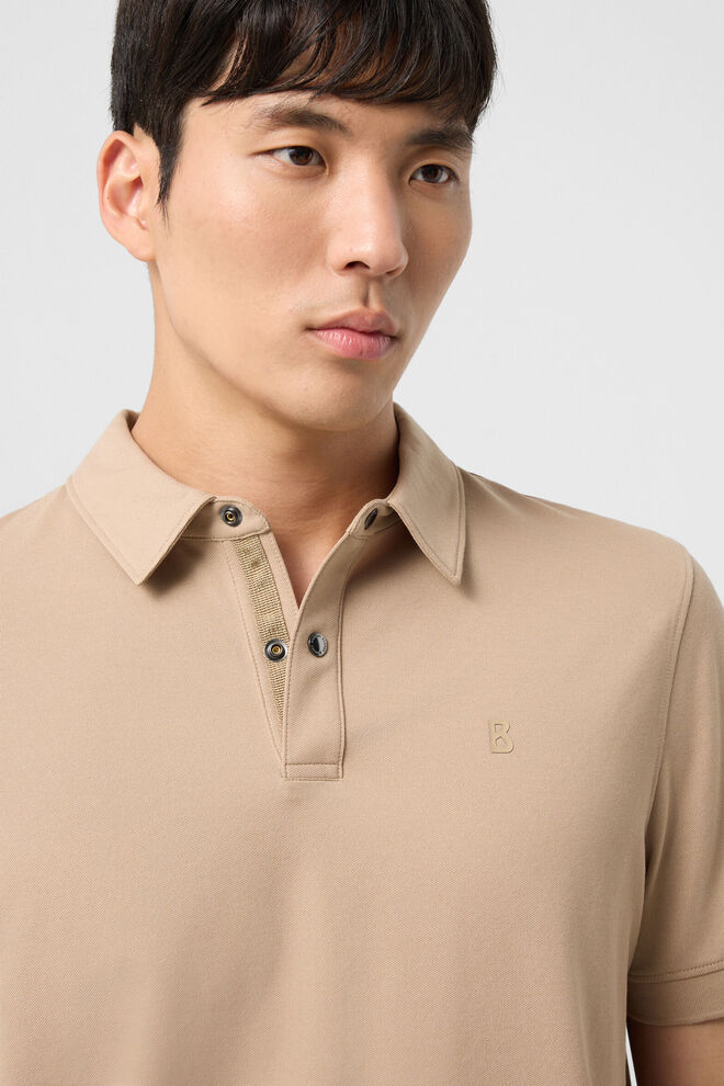 Das Herrenmodell tr&auml;gt das beigefarbene Polo-Shirt Timo, das mit einem dezenten Logodetail auf der Brust akzentuiert ist.