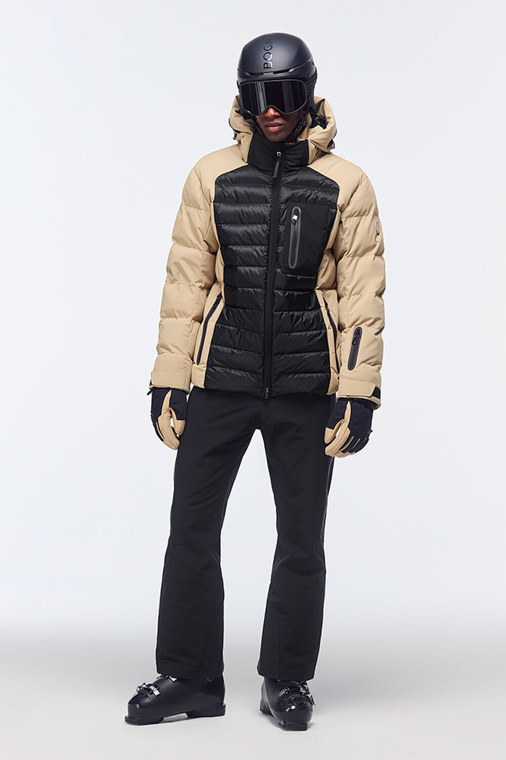 The model is wearing a ski look in Black/Beige with a black ski helmet, ski goggles and ski boots.