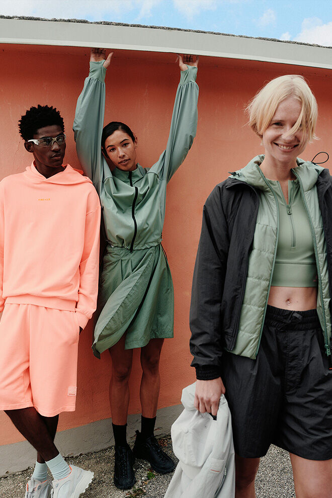 A group of three models in relaxed poses. They are wearing FIRE+ICE looks in bright orange and the trend colour eucalyptus.