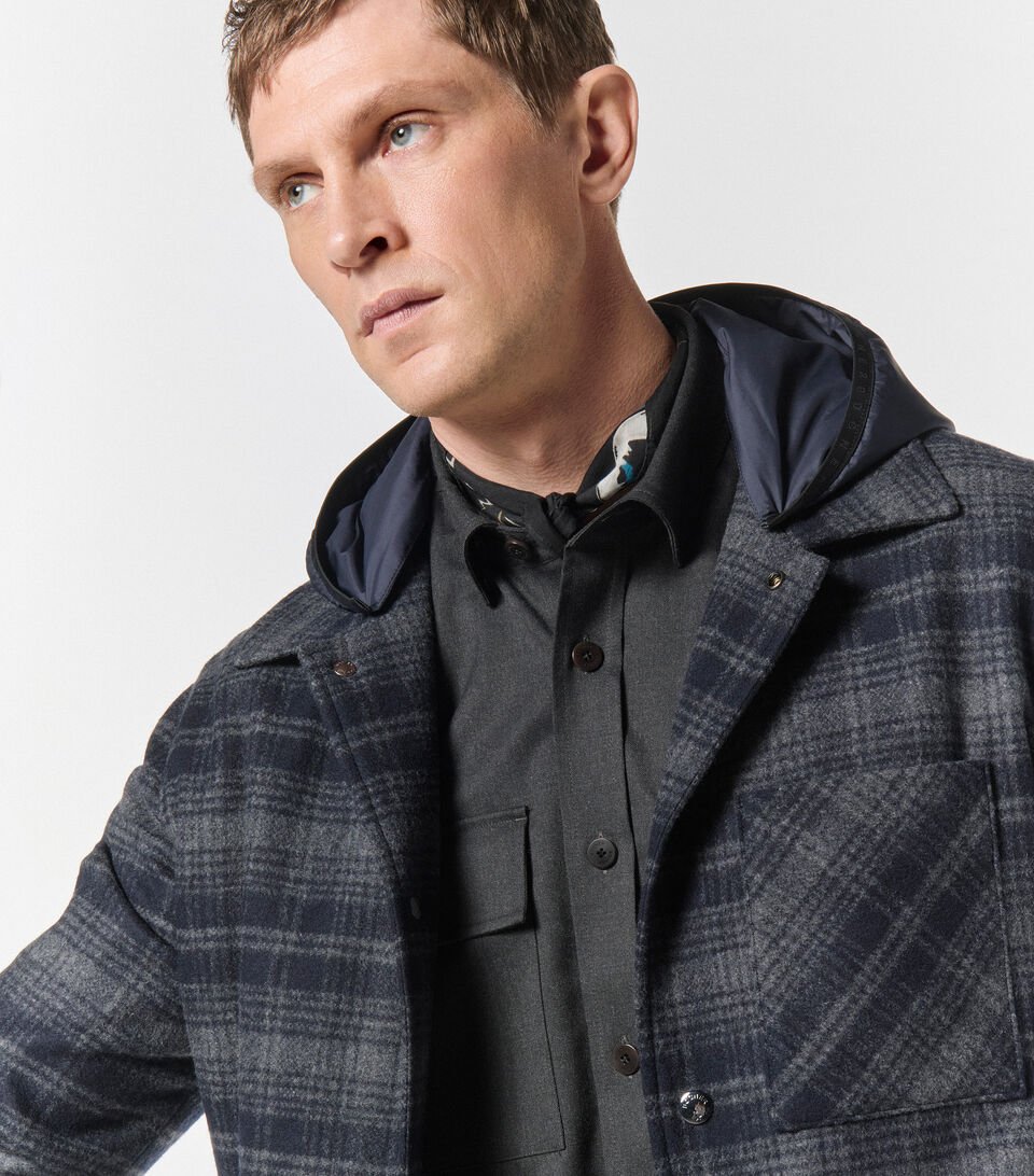 Close-up of a male model wearing a grey and blue checked shirt jacket in wool, with a grey woollen shirt underneath. 