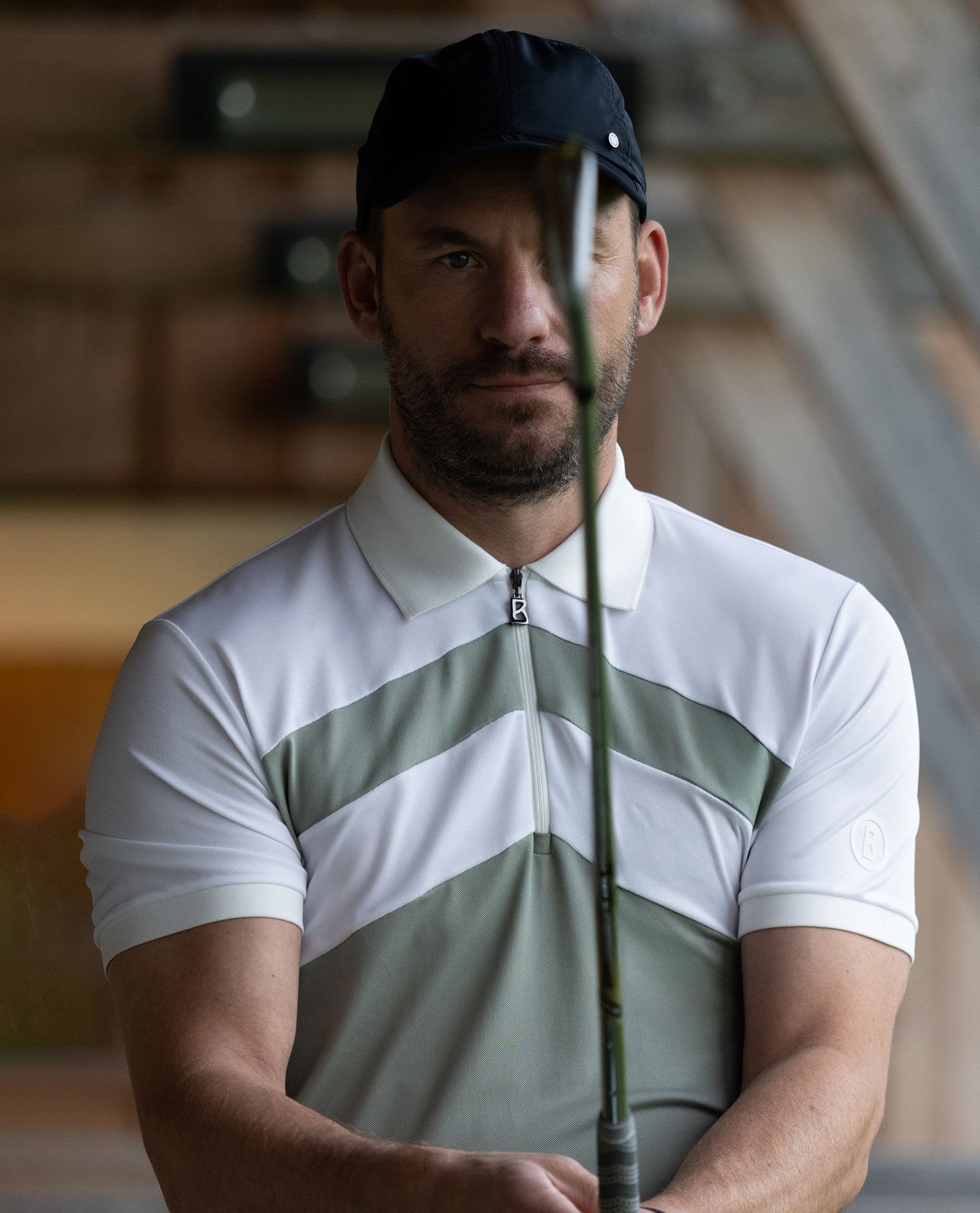 Front view of a golfer with a golf club. He is wearing a green and white polo shirt with a striped pattern.