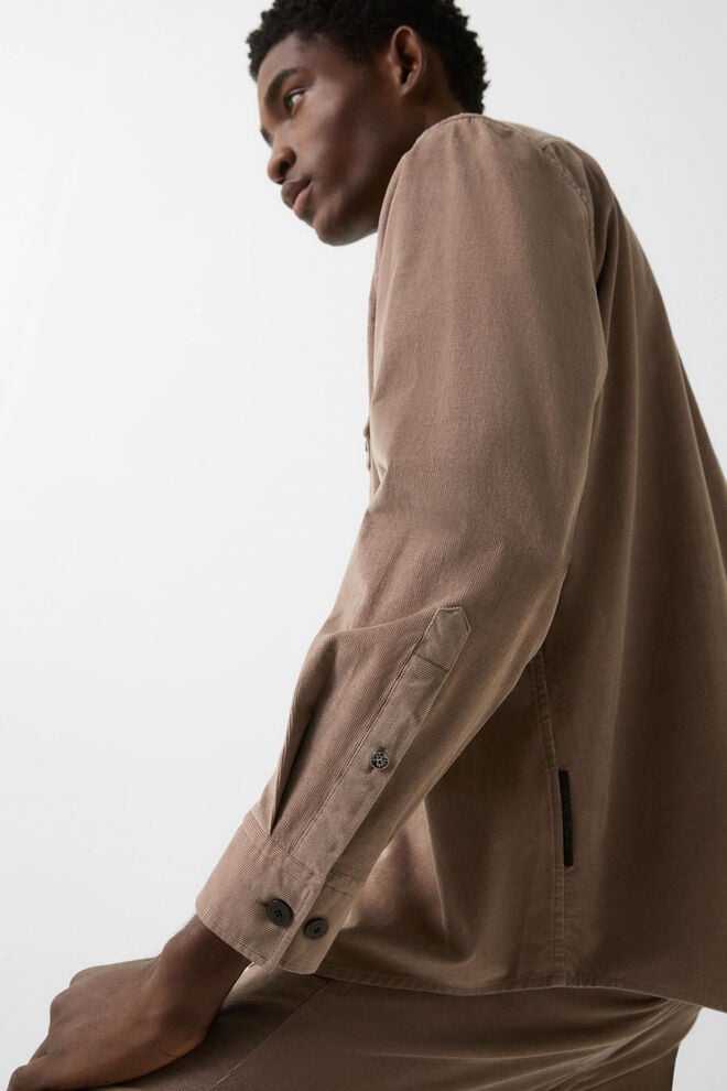 Seitliche Ganzk&ouml;rperaufnahme. Im Hintergrund eine Bergkulisse. Das Damen Model tr&auml;gt einen hellen Ski-Anzug und Handschuhe.