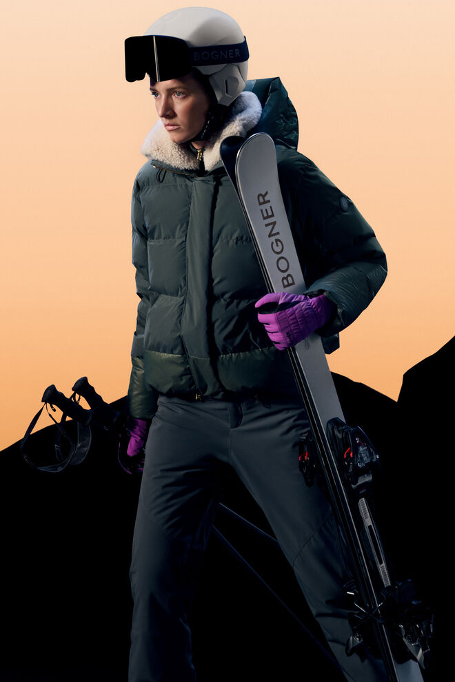 Aufnahme des anderen Damen Models mit Daunenjacke Maja in Eukalyptus. Sie h&auml;lt Ski und St&ouml;cke in der Hand.