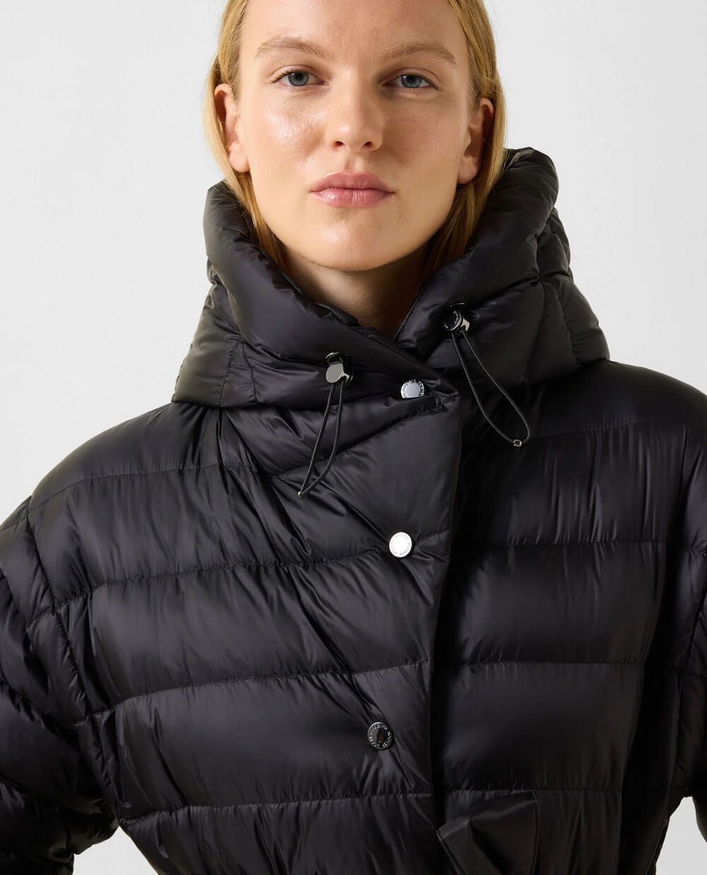 The model is wearing the Milly down jacket with a voluminous hood and an exclusive tie at the waist.