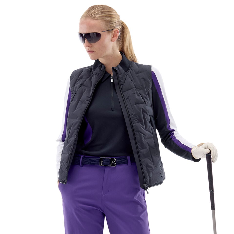 Das Damen-Model trägt eine leicht Daunenweste in Schwarz, dazu einen First Layer sowie eine Funktionshose mit Gürtel.