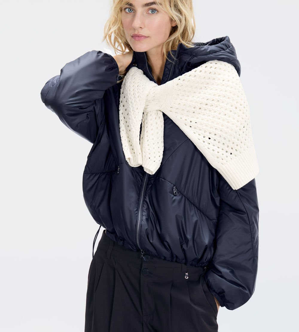 The female model is wearing a lightweight, padded Beryll jacket in dark blue, with a white eyelet-knitted pullover.