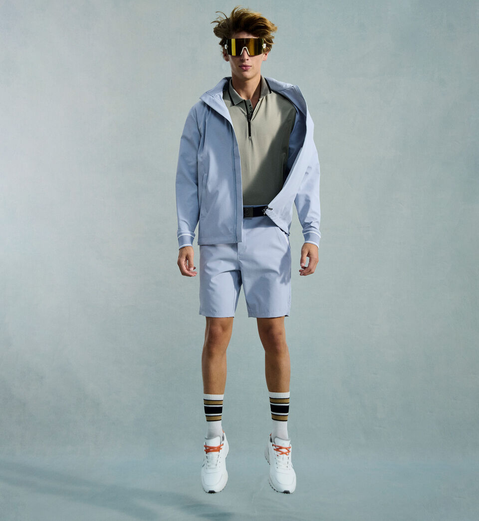 The male model is dressed in a green polo shirt, paired with a light blue blouson jacket and matching shorts.