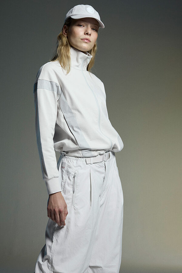 Seitliche Aufnahme des Damen Models. Sie tr&auml;gt eine Zipperjacke mit Stehkragen, dazu Softshell-Hose Charis.