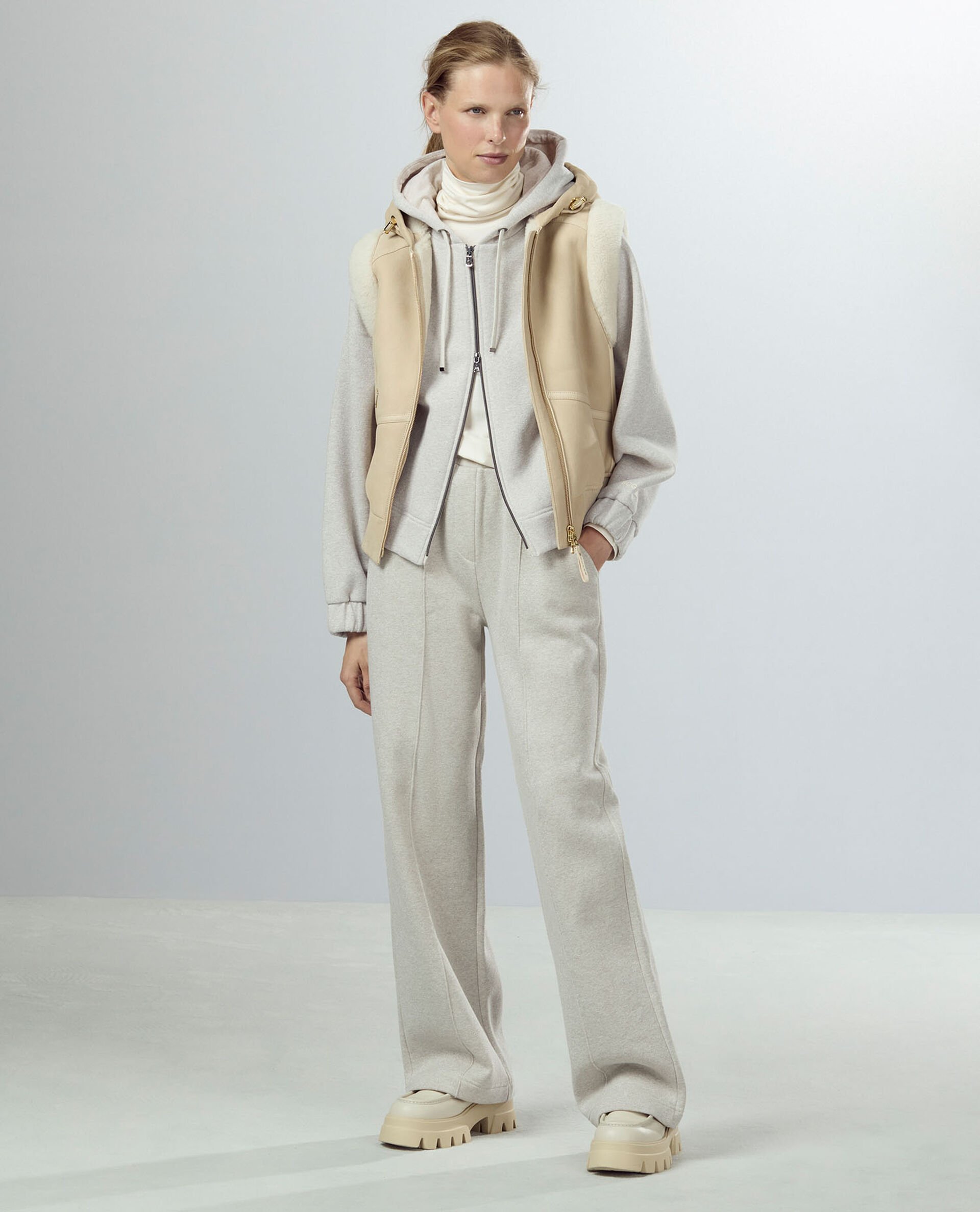 Das blonde Damen Model trägt einen Sweat-Anzug in Hellgrau, dazu beigefarbene Plateau-Loafers und eine Lederweste. Das blonde Damen Model trägt einen Sweat-Anzug in Hellgrau, dazu beigefarbene Plateau-Loafers und eine Lederweste.