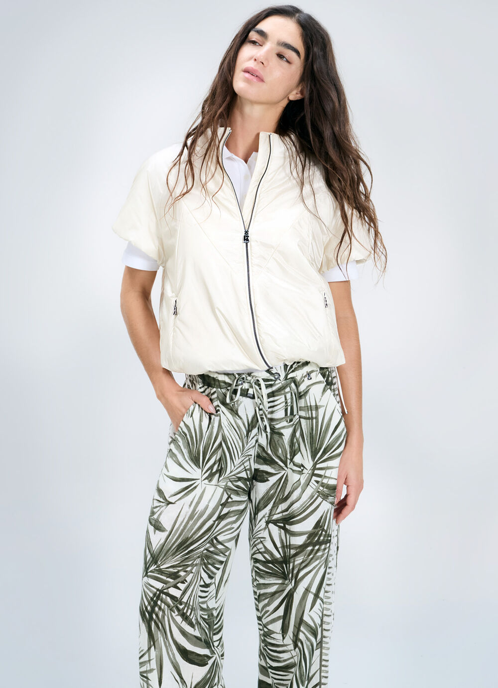 Das Damen Model tr&auml;gt eine extraleichte kurz&auml;rmelige Jacke, darunter ein Polo-Shirt und eine luftige Hose mit Palmen-Print.