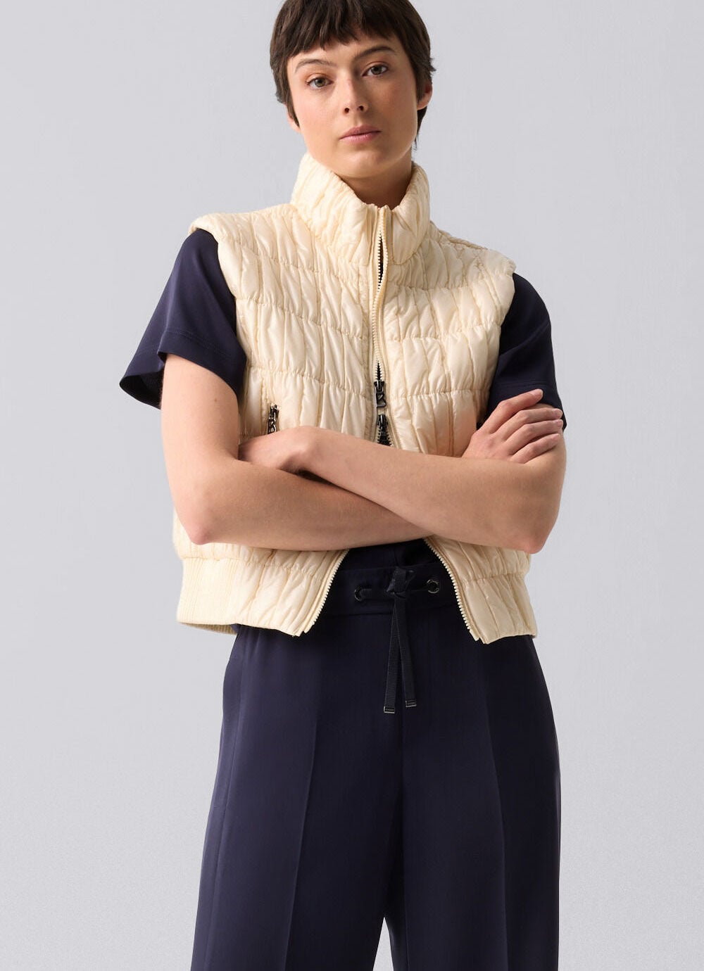 The female model wears a matching set consisting of shirt in pants in navy blue. A cream-colored vest with quilted pattern rounds off the look.