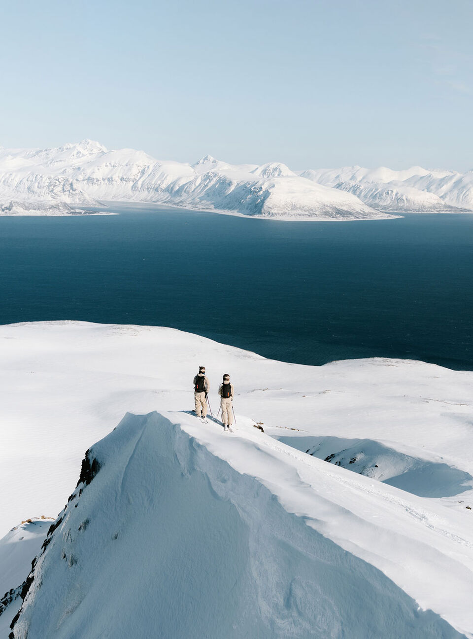 Ausblick auf eine schneebedeckte Landschaft in Norwegen. Die beiden Models tragen Ski-Anz&uuml;ge von FIRE+ICE in Beige und Schwarz.