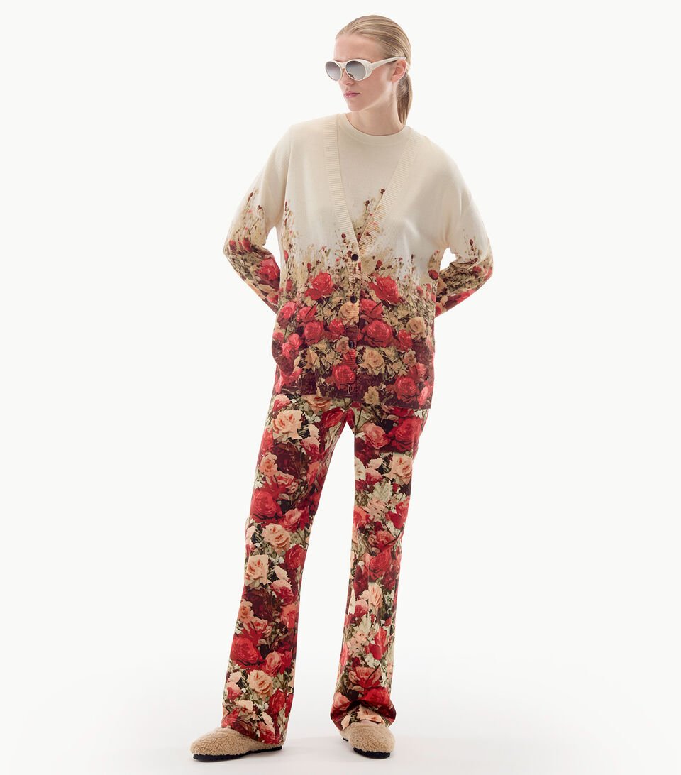 The model is styled in beige trousers and a beige cardigan boasting a red floral pattern, complemented by sunglasses.