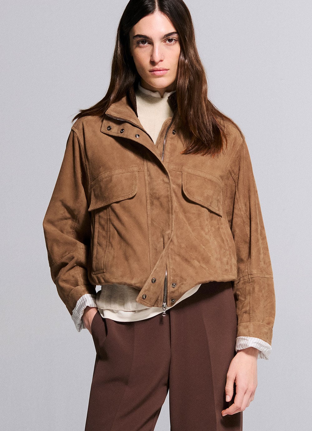 Das andere Damenmodell tr&auml;gt eine camelfarbene Velourslederjacke, darunter ein gestricktes Oberteil und eine braune Hose.