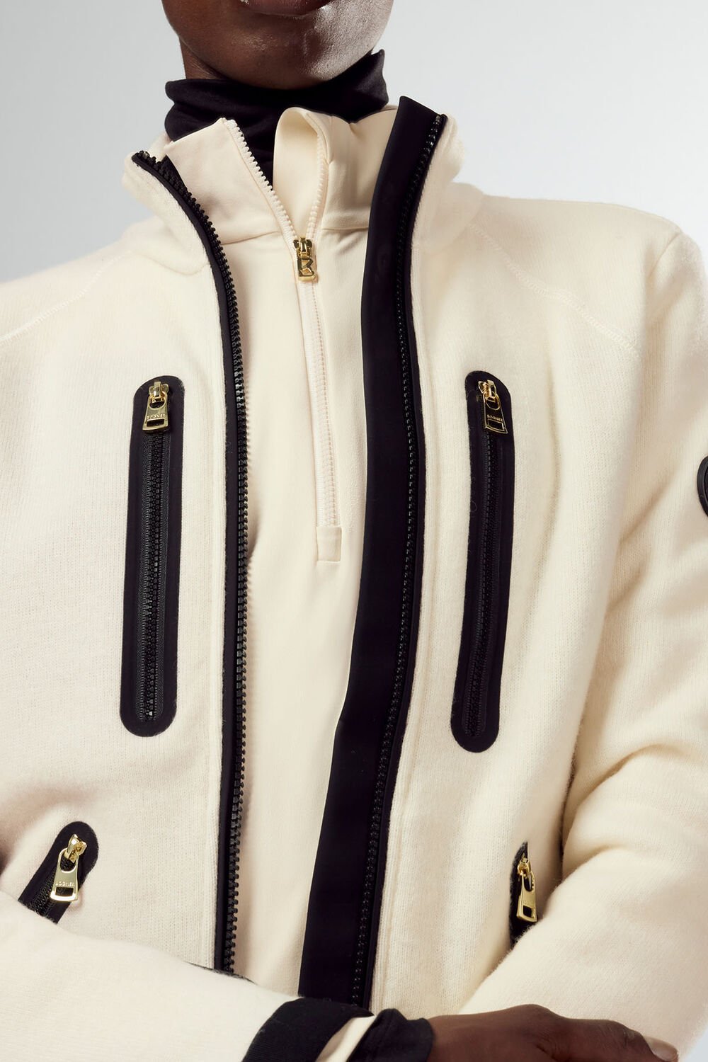 Close-up von Mid Layer Charlot aus Tech-Wolle. Kontrast-Einsätze in Schwarz und goldfarbene Details runden das Design ab. Close-up von Mid Layer Charlot aus Tech-Wolle. Kontrast-Einsätze in Schwarz und goldfarbene Details runden das Design ab.