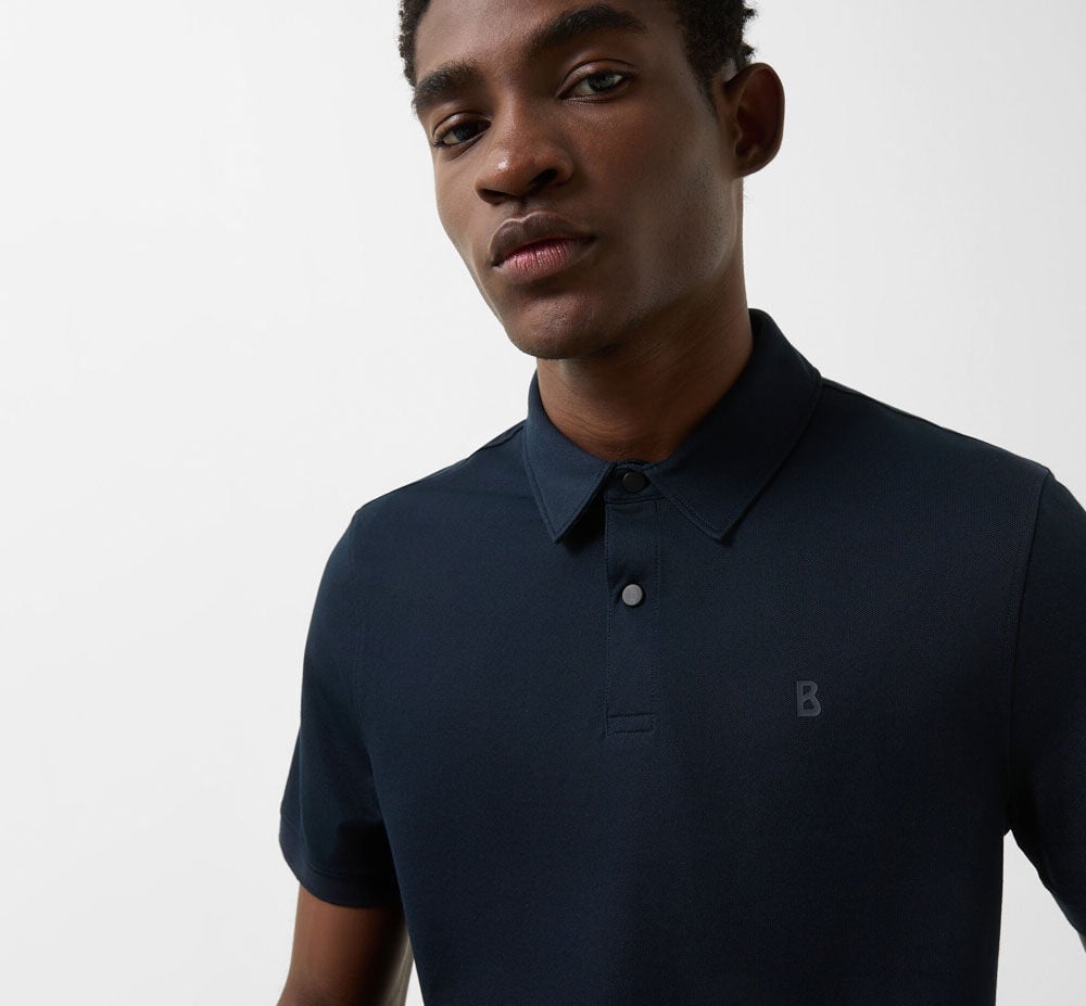 Close-up des Herren Models im dunkelblauen Polo-Shirt. Es hat eine kurze Knopfleiste und ein B-Logo.