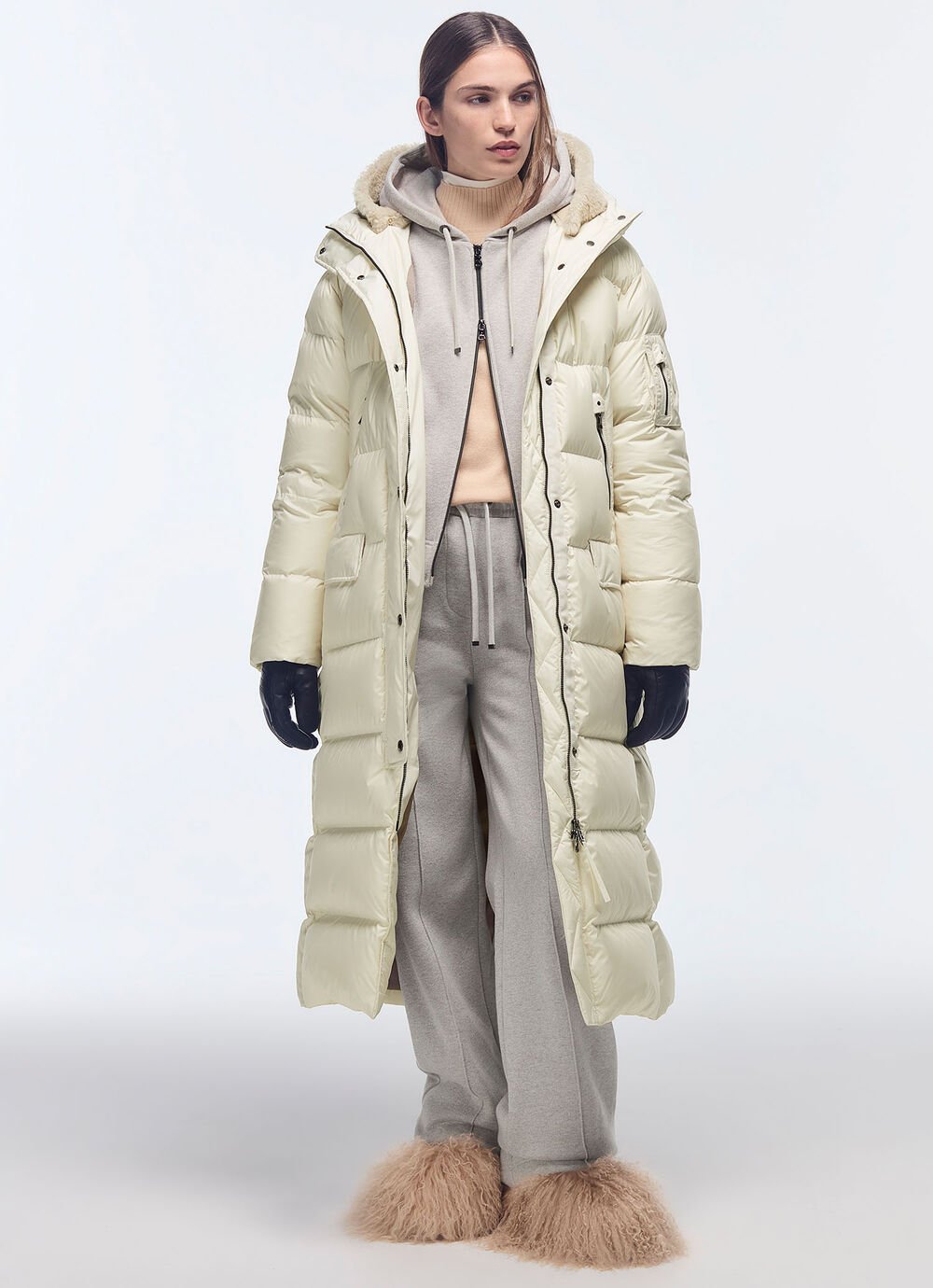 Dieser Look besteht aus einem langen Daunenmantel, unter dem ein Rollkragenpulli, ein graues Set sowie Fellboots getragen werden.