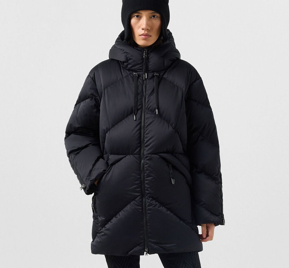 Dark-haired women's model wearing the black Glenda down parka, matching pants and a black hat.