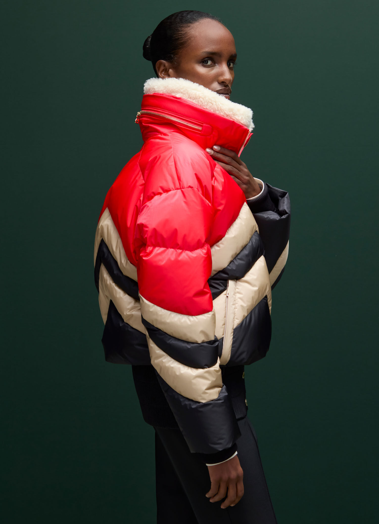 Het vrouwelijke model draagt een zwart met rood en beige donzen ski-jas met een groot doorgestikt W-patroon.