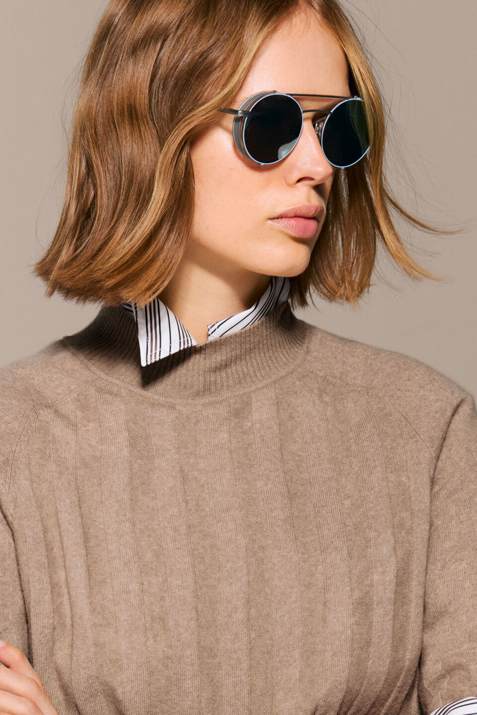The female model is wearing the striped Gigi blouse underneath the Tina virgin wool shirt in camel beige.
