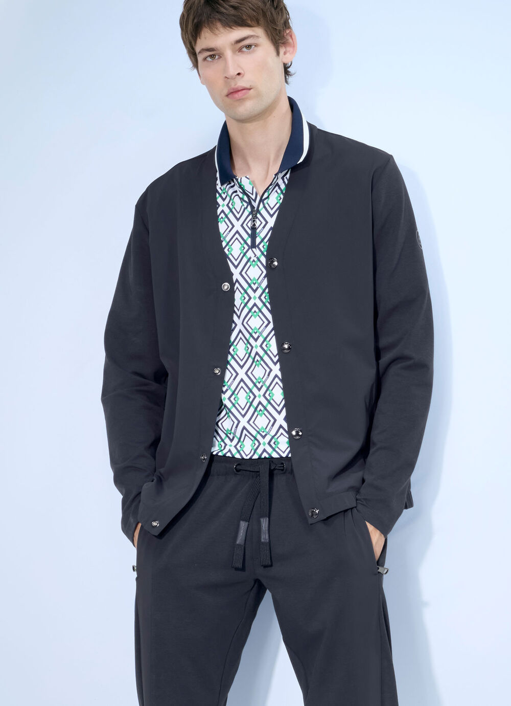 The male model wears a dark blue blouson jacket and golf pants. Underneath is a polo shirt with a distinctive graphic &lsquo;B&rsquo; print.
