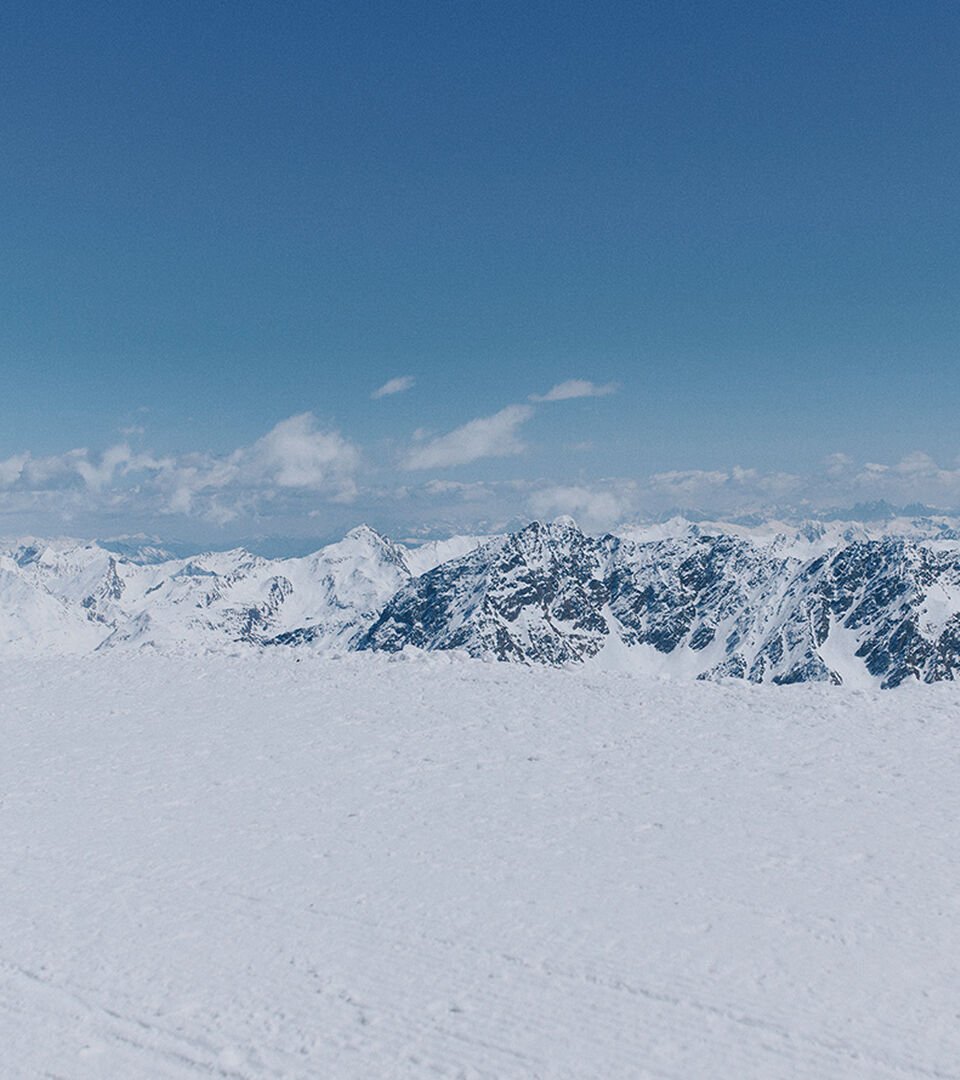 Das mit einer Skijacke bekleidete Model steht vor einer schneebedeckten Bergkulisse.