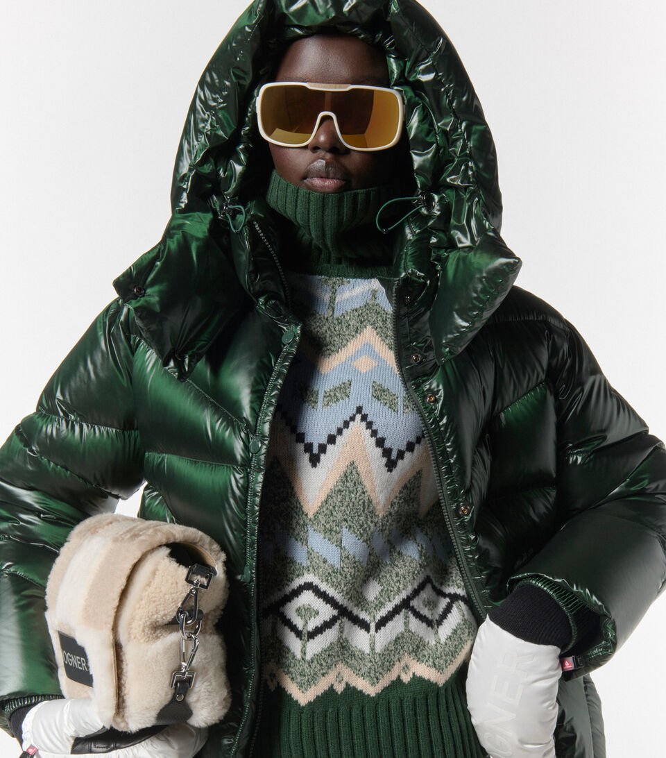 Close-up of female model. She is wearing a dark green, shiny down jacket, a Norwegian sweater and sunglasses. Close-up of female model. She is wearing a dark green, shiny down jacket, a Norwegian sweater and sunglasses.